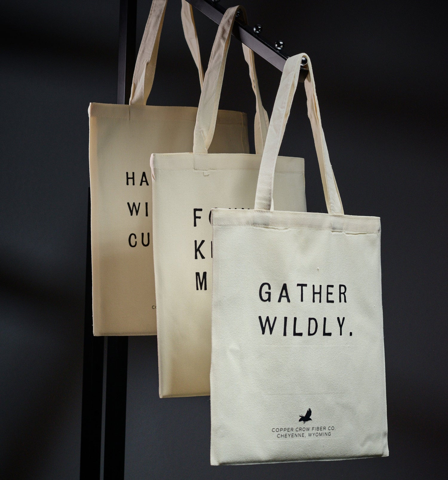 Three tote bags with text and branding on a dark background