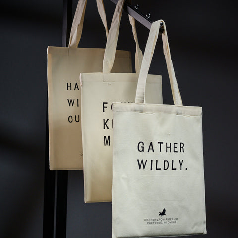 Three tote bags with text and branding on a dark background