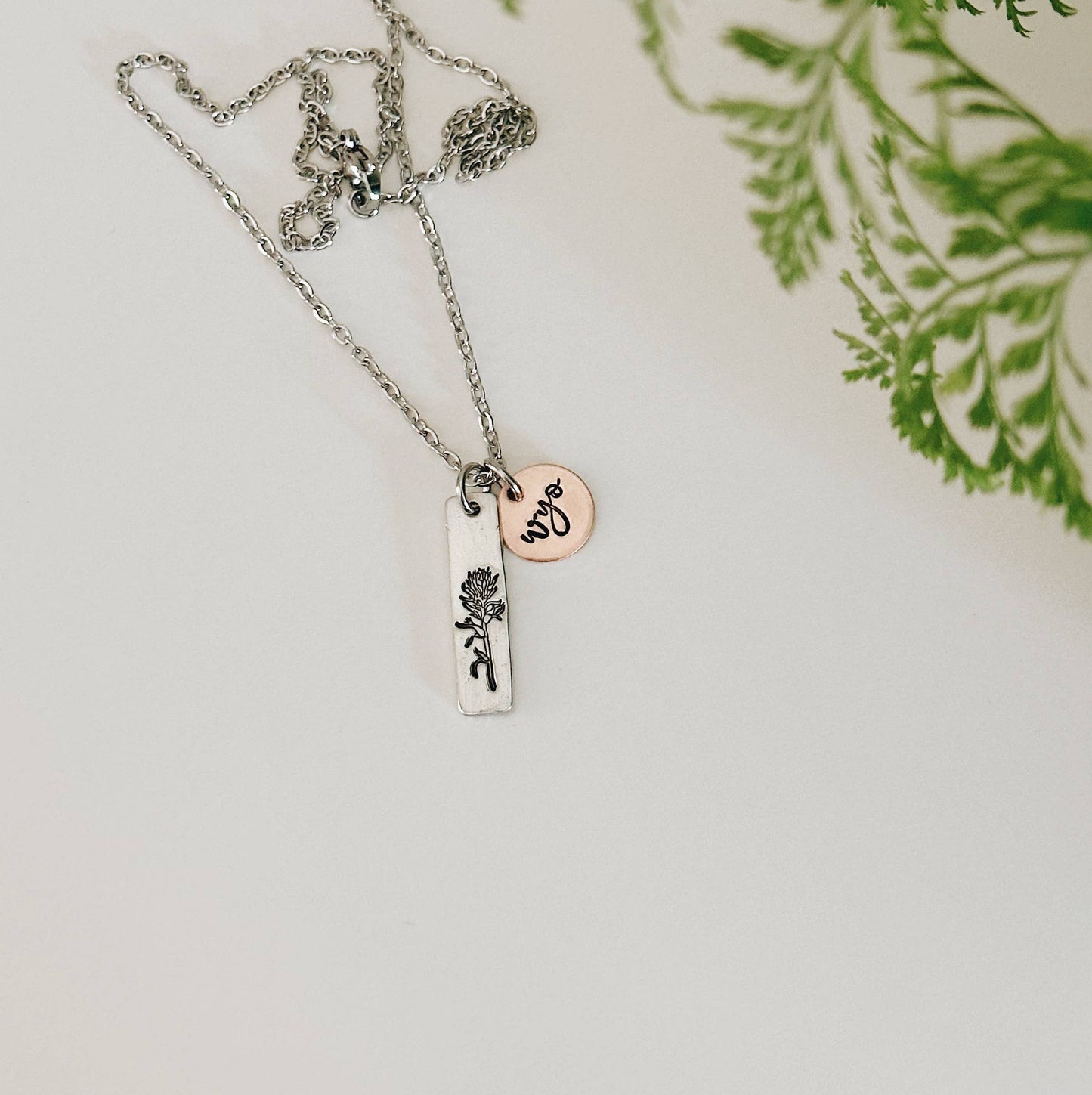 Necklace with two pendants on a light background. One is hand-stamped with an Indian Paintbrush flower and the other with "wyo" in a script font.