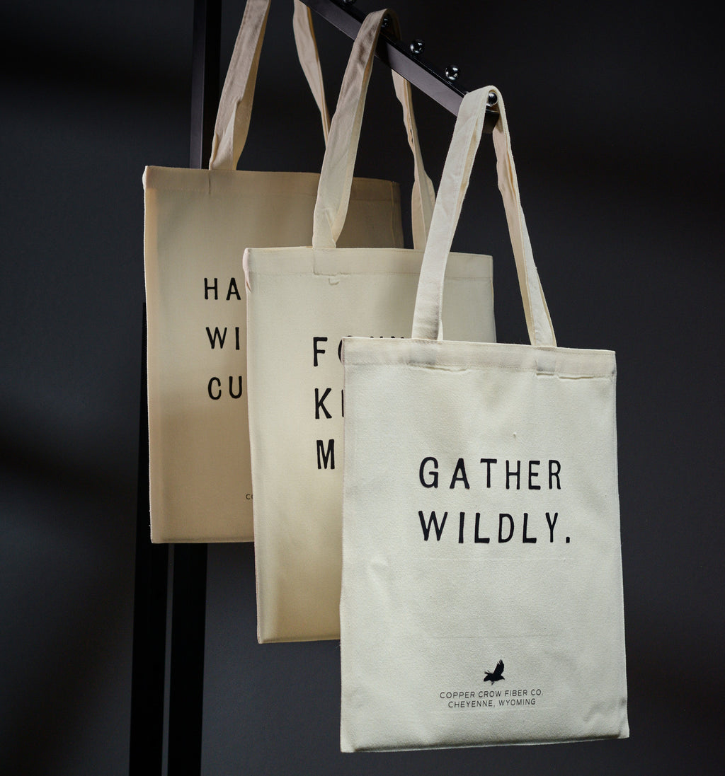 Three tote bags with text and branding on a dark background
