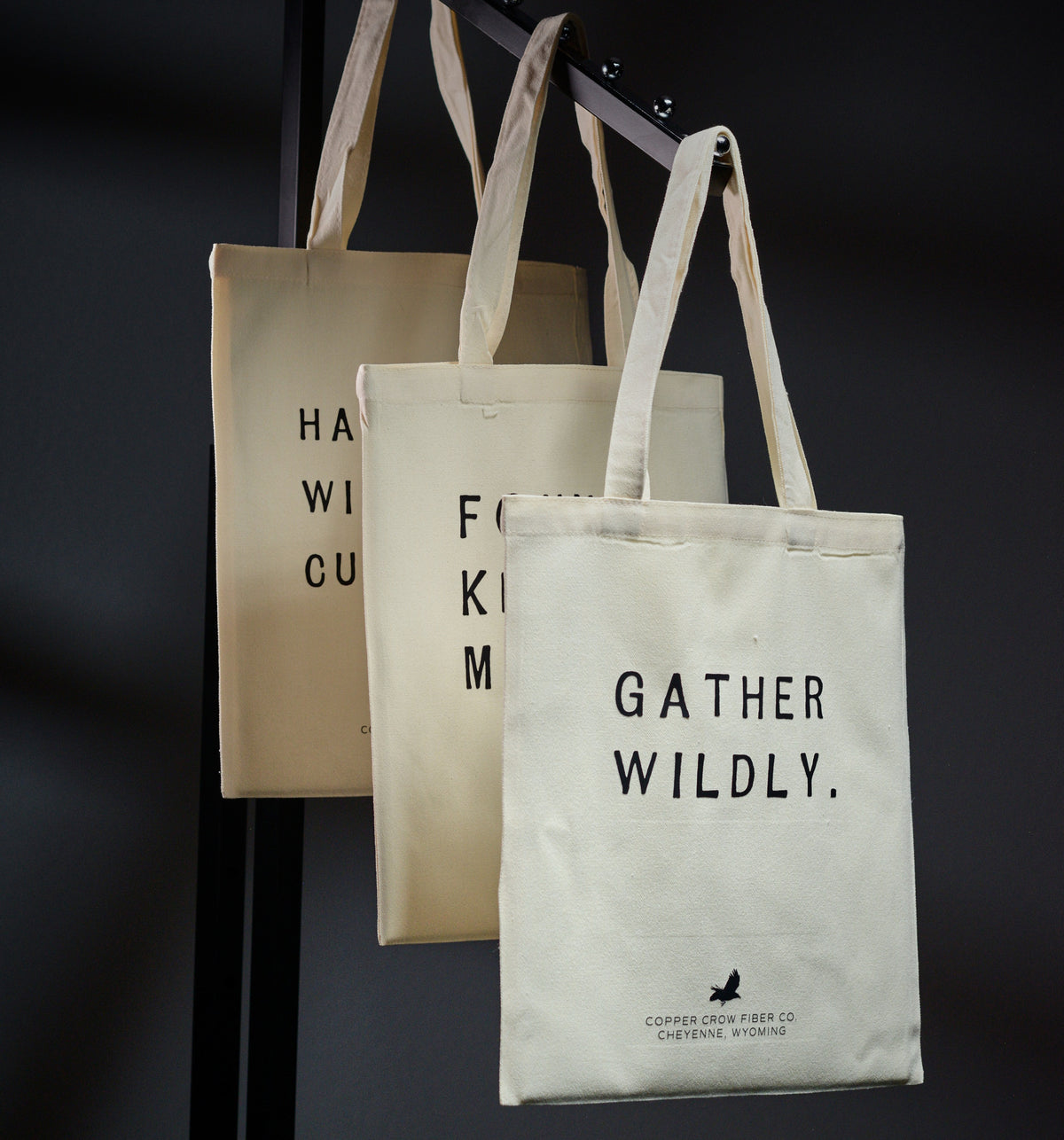Three tote bags with text and branding on a dark background